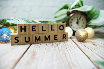 Hello Summer alphabet letter with alarm clock and Monstera leave decoration on wooden background