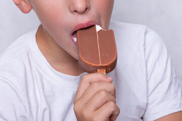 A boy whose face is unrecognizable eats ice cream covered in chocolate. - obrazy, fototapety, plakaty