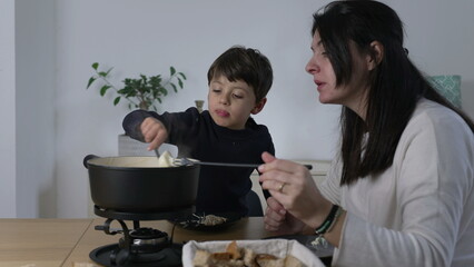 Mother and Child Sharing Swiss Fondue, Enjoying Cheese and Bread Together, eating traditional...