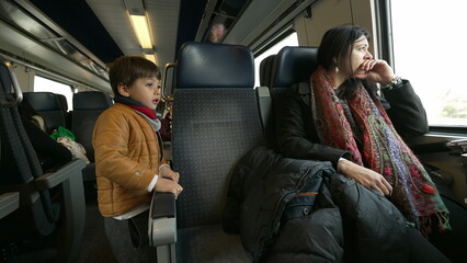 Mother and child traveling by train together, little boy standing on corridor while mom stares out...