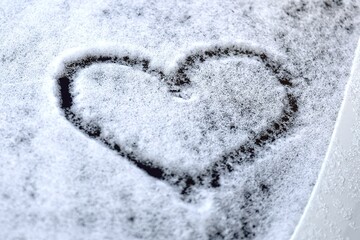 Heart shape symbol drawn on snowed car glass. 