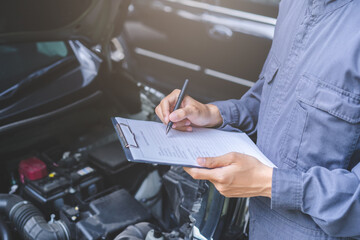 Auto check, car service shop concept. Automobile repairman writing job checklist on clipboard, mechanic checking engine to estimate repair machine, inspecting maintenance by engineer at vehicle garage - Powered by Adobe