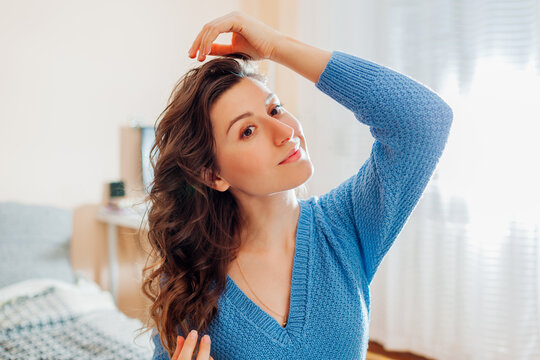 Portrait of woman checks her hair after heatless hair curler at home. Beauty products for wavy hairstyle.