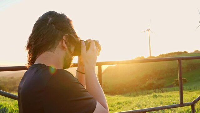 Man with long hair taking pictures of wind towers at sunset