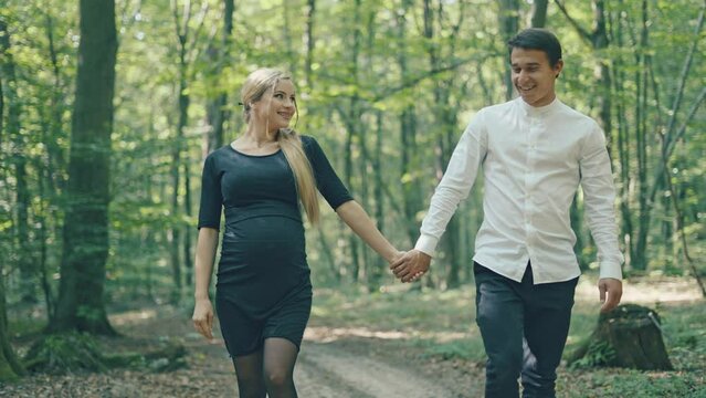 Young pregnant woman and her husband having fun in park. Happy family outdoors. Expecting for firstborn	