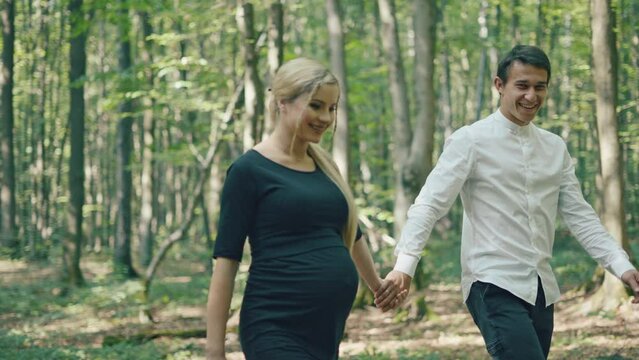 Young pregnant woman and her husband having fun in park. Happy family outdoors. Expecting for firstborn	