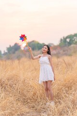 Beautiful Girl in White Dress Holding a Colorful Windmill Toy in a Dry Grass Meadow