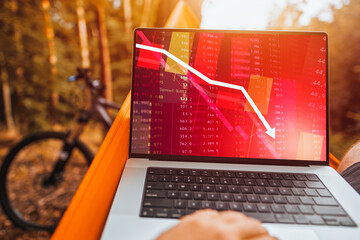 A Freelancer Trading Crypto in the Park with a modern Laptop and Enjoying the Red Market Crash. Bad day in crypto asset trading.