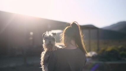 Woman, dog and outdoor with back in nature, countryside and hug by house, field or land in sunshine. Girl, puppy or animal pet for embrace, care or love for bonding on walk, adventure or home by hill