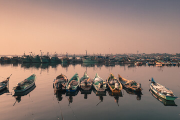 Boats in the harbor tide with the rope where many fishing boats seen behind at the colorful morning sky with perfect reflections at chennai tamilnadu India - obrazy, fototapety, plakaty