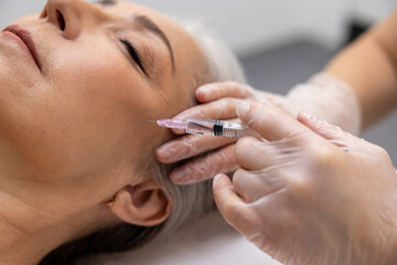 Beautician doing filler injections to a mature female patient