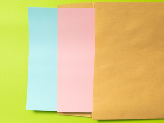 kraft envelope with pink and blue paper sheets on a green background. Recycled paper envelope