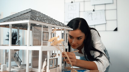 Fototapeta na wymiar Young beautiful caucasian architect engineer turns house model around to inspect house construction and check mistake point to solve the problem on meeting table at modern office. Closeup. Immaculate.