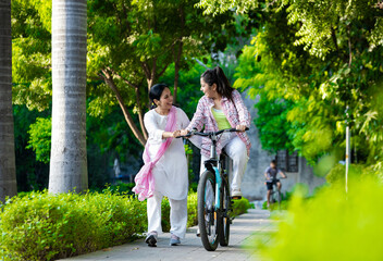 Mother helping daughter in cycling in Outdoor Garden, Mother and daughter Bonding , - obrazy, fototapety, plakaty