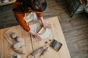 Woman potter in her workshop, rolling out clay. Skilful female artisan at work, rolling white clay...