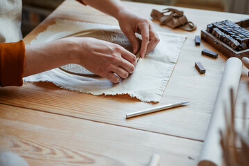 Female potter's hands mould the edges of a clay plate in the workshop. Pottery, hand moulding a...