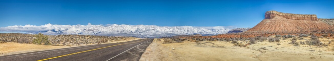 Panoramic picture of a lonely road through desert with snow covered mountains