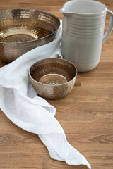 Water pitcher, copper bowls of water and a white linen cloth on a wood table