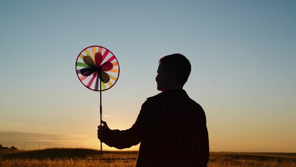 Child boy play with toy wind pinwheel in his hand on summer field at sunset. Happy child boy plays...