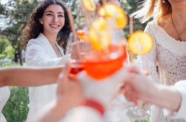 Close up of young women holding elegant glasses with long stem of alcohol cocktails and clink them.