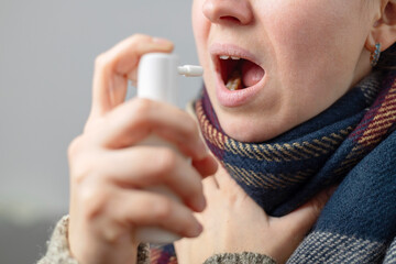 A woman with a sore throat sprays medicine aerosol spray down her throat