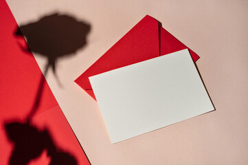 Blank paper card mockup and red envelope on pastel pink and red background with harsh sunlight...