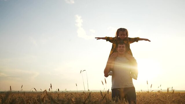 the child sits on father shoulders. happy life and family for child concept. a little girl spreads her arms to the sides and sits on her father shoulders, a man walks through the field lifestyle
