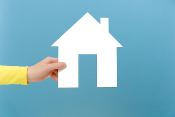 Fototapeta na wymiar Closeup of female hand holding white paper house, concept of dream home purchase, mortgage, real estate insurance, repairing service concept, posing isolated over blue color background wall in studio