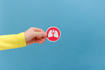 Close up of female hand holding lungs symbol, posing isolated over plain blue color background wall...