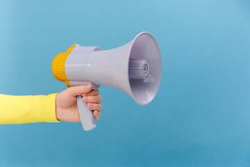 Closeup of woman hand holding megaphone, announcing of advertisement or protesting, posing isolated over plain blue color background wall in studio with copy space for promotion content or design