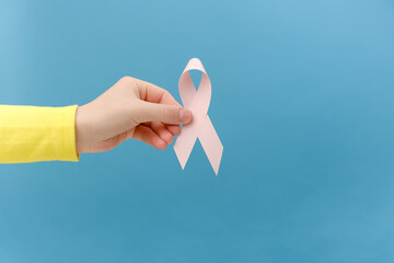 Closeup of female hand holding small pink ribbon, symbol of breast cancer awareness, oncological...