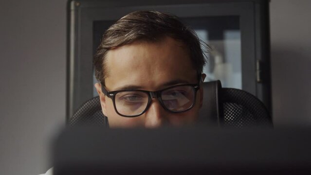 Young adult man in glasses working on laptop. The camera moves