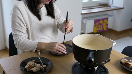 Swiss Fondue Feast, woman Enjoying Bread and Cheese at Home. homemade traditional European dish in...