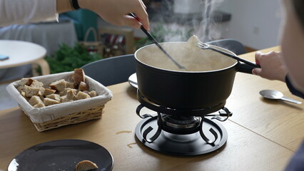 Traditional Swiss Fondue - people eating pieces of bread with cheese at home, close-up of European...