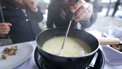 Traditional Swiss food, closeup hand holding fork with bread dipping in cheese, peopel enjoying...