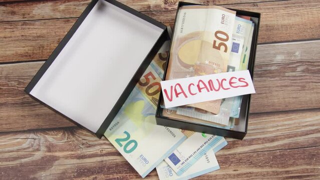 boite rempli de billets de banque avec un papier avec écrit dessus "vacances" en français