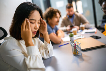 Young Asian business woman having headache in the office while having a meeting