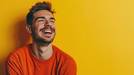 Fototapeta premium A young man in an orange shirt laughs joyfully against a yellow background, capturing a moment of genuine happiness and carefree spirit.