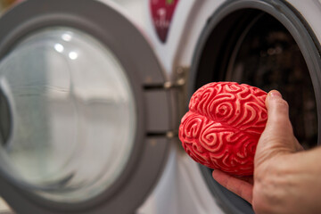 Hand Putting a Rubber Brain in a Washing Machine, Brainwashing Concept.