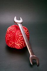 Wrench on top of a red brain with a dark green background. Concept of psychology helps the brain.