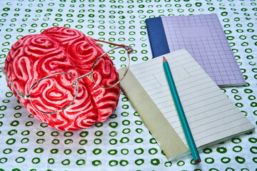 Representation of a red brain learning as artificial intelligence, with some books and a pen with a white background with green circles.