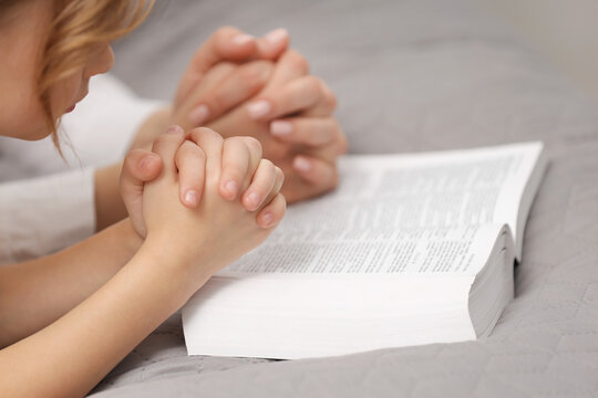 Girl and her godparent praying over Bible together indoors, closeup. Space for text