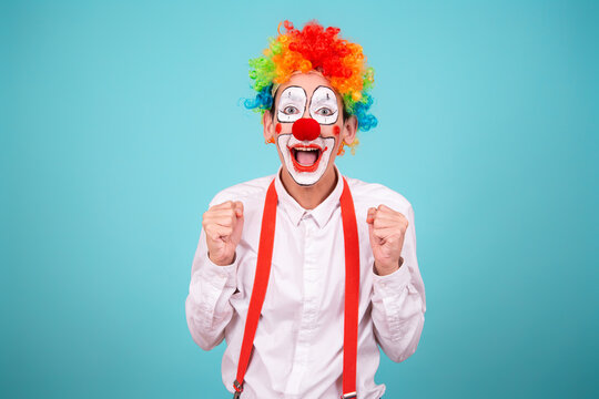 A joyful clown. A cute man in a suit and makeup for a holiday for children. A fool. Blue background. Copy the space.