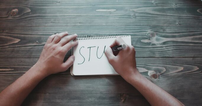 Top view, close-up hands of a man writing STUDY.