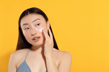 Beautiful young woman with sun protection cream on her face against orange background, space for...
