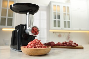 Electric meat grinder with minced beef on white marble table in kitchen. Space for text