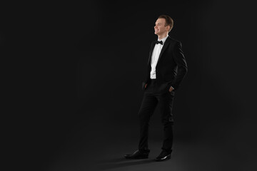 Handsome young man in stylish suit on black background, space for text