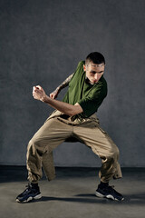 Graceful male with tattooed body, earrings, beard. Dressed in khaki t-shirt, jumpsuit, black...