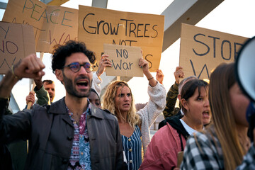 Serious multiracial group demonstrating against the war and violence in the world. People gathered with written banners with messages to grow trees not armies and anti-war
