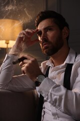 Handsome man smoking cigar at home in evening